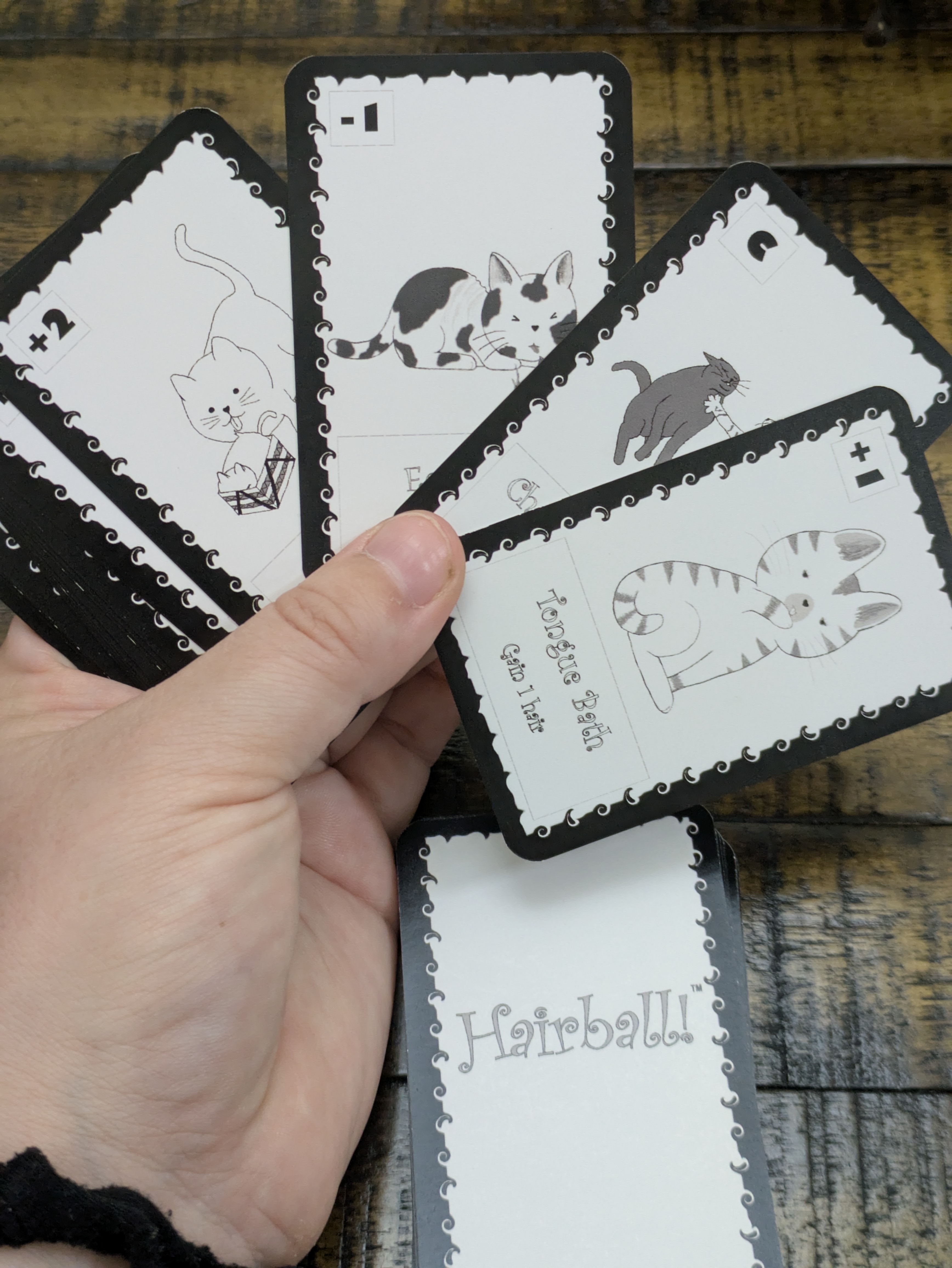 A hand holding a fan of Hairball! cards